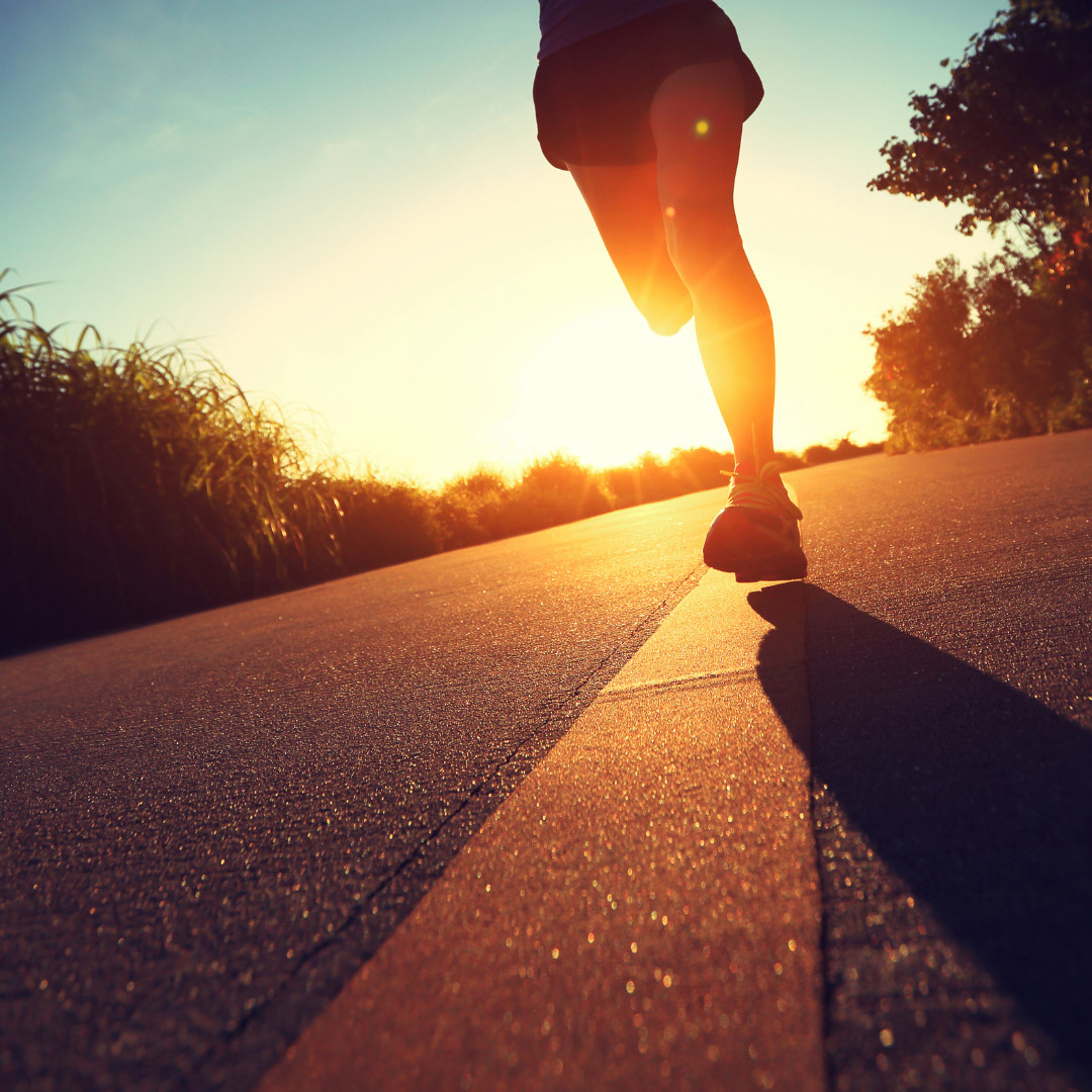 Closeup of runner's legs as they sprint down a road at sunrise